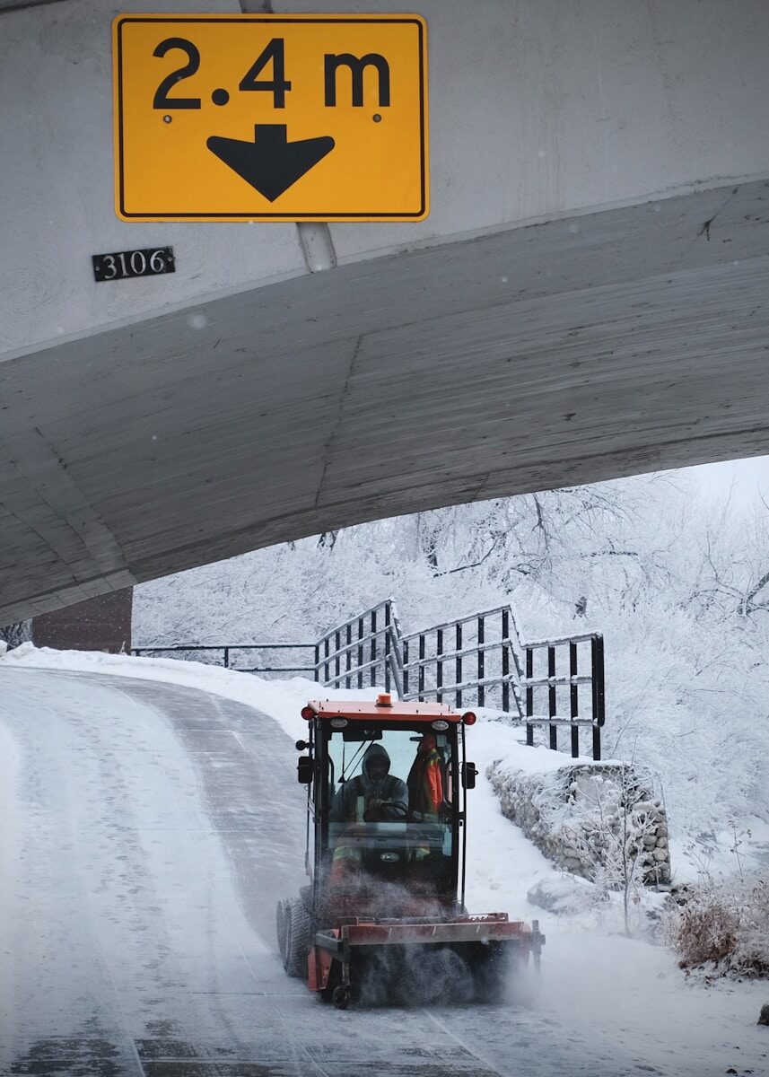 A snowplow clears a snowy road under a bridge.